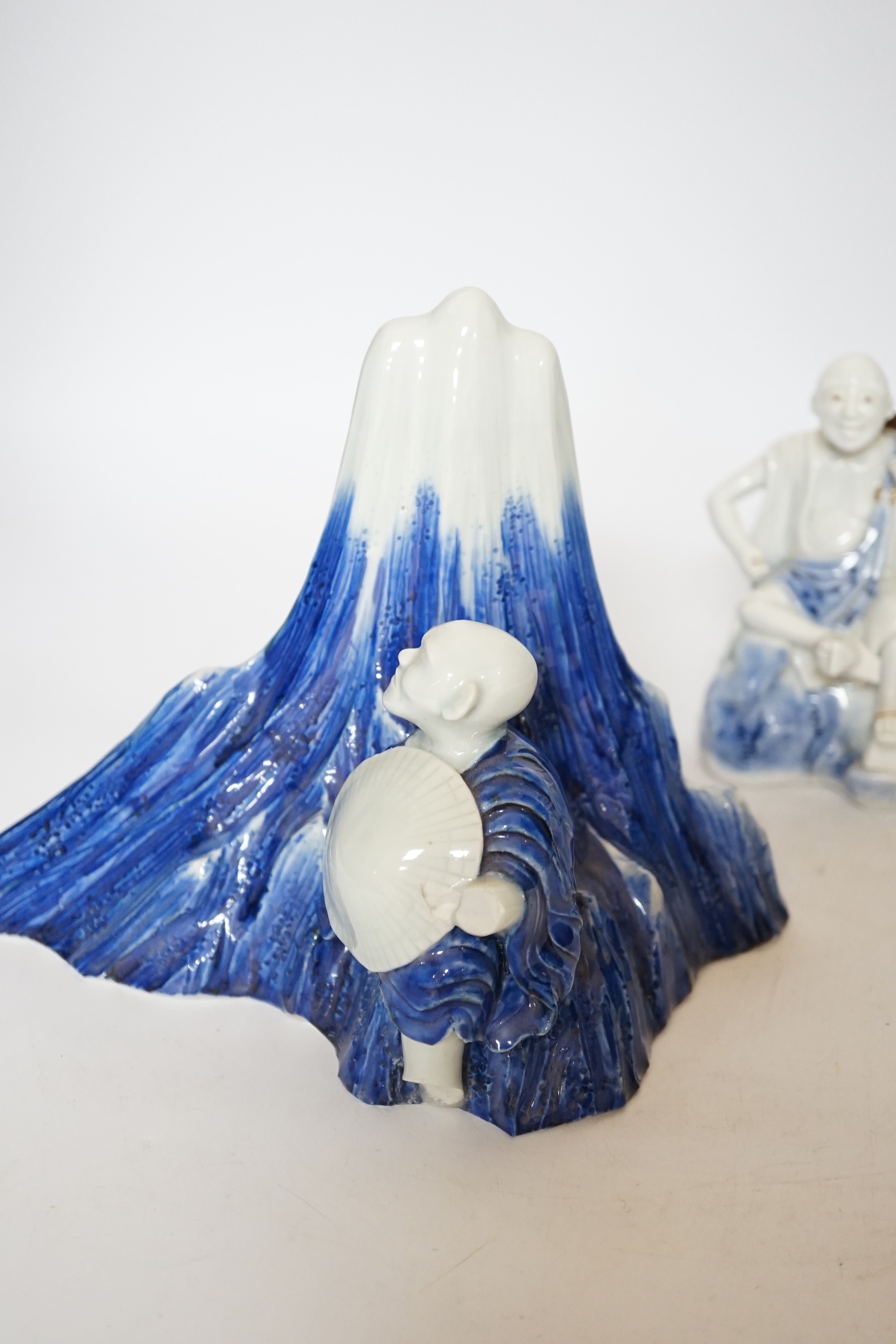 An early 19th century Japanese Hirado blue and white model of a monk seated by Mount Fuji, and a similar brush pot modelled with a fisherman seated by the cylindrical vessel, largest 17cm high (2)